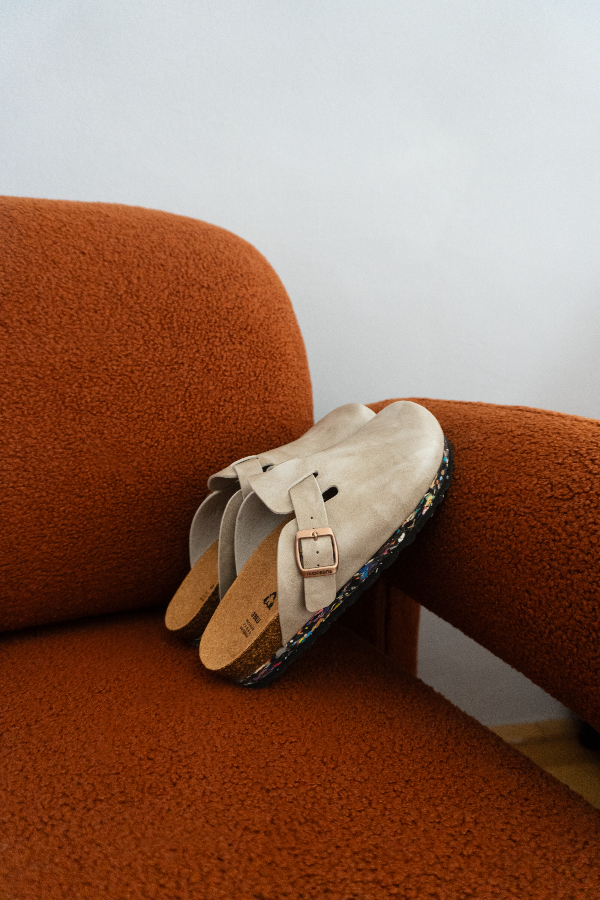 Pair of light grey shoes with a buckle on an orange chair against a white wall